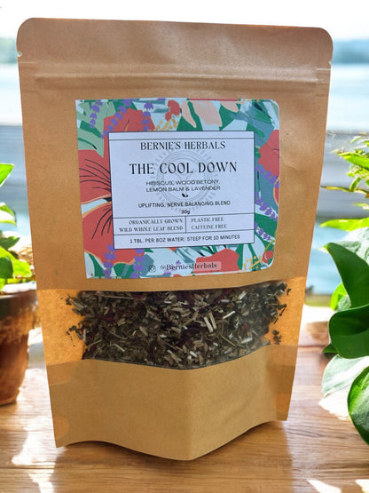 A floral-patterned paper bag labeled 'The Cool Down - Nervous System Support' containing dried herbs for tea.