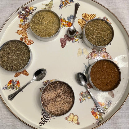 Decorative plate with four small bowls of spices and spoons on a textured surface